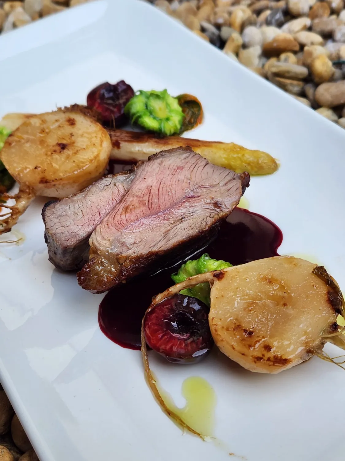 Bœuf rosé, pommes de terre et jus sombre dans une assiette rectangulaire blanche