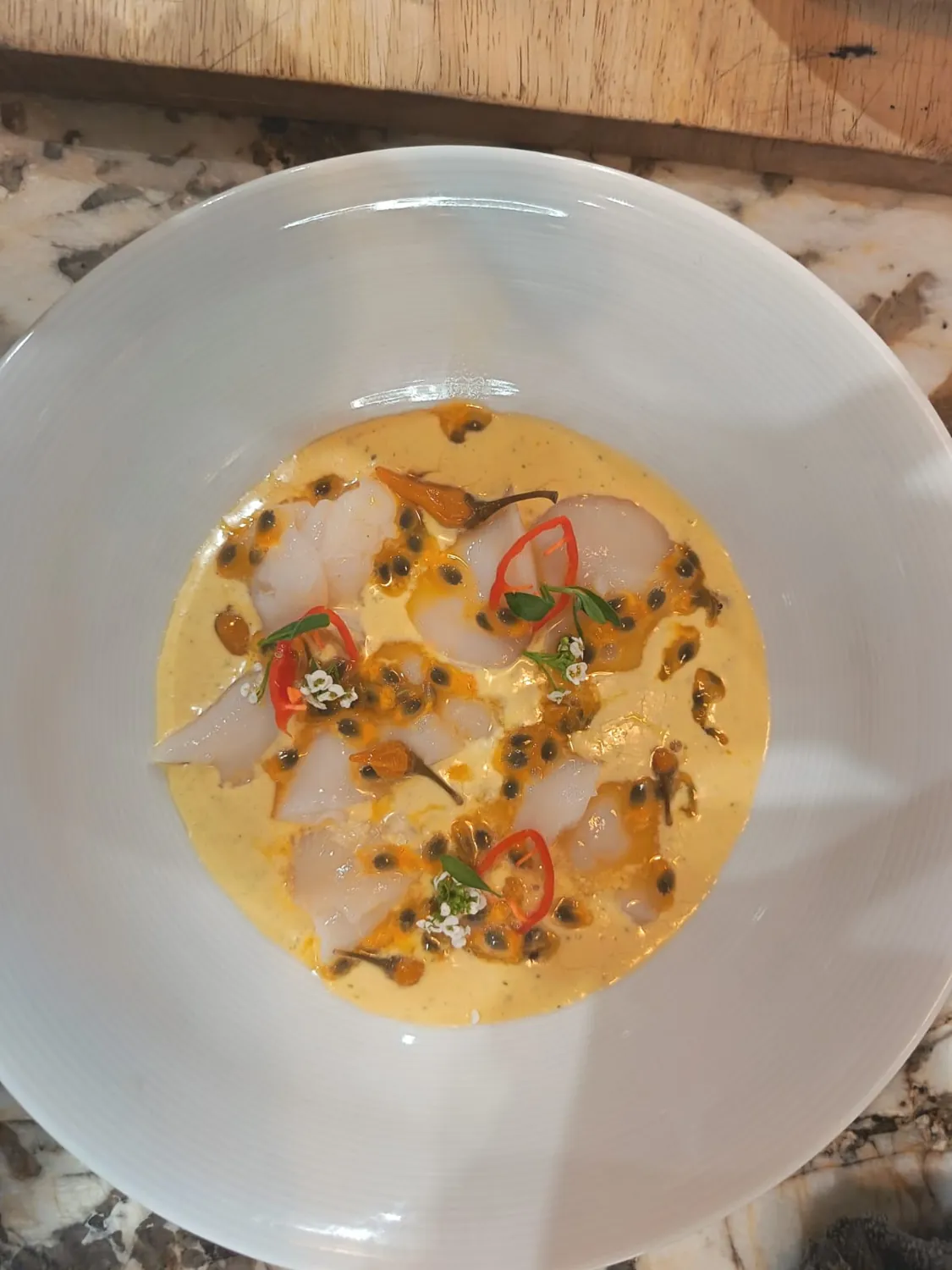 Poisson cru en fines tranches, sauce jaune, graines de fruit de la passion et piment