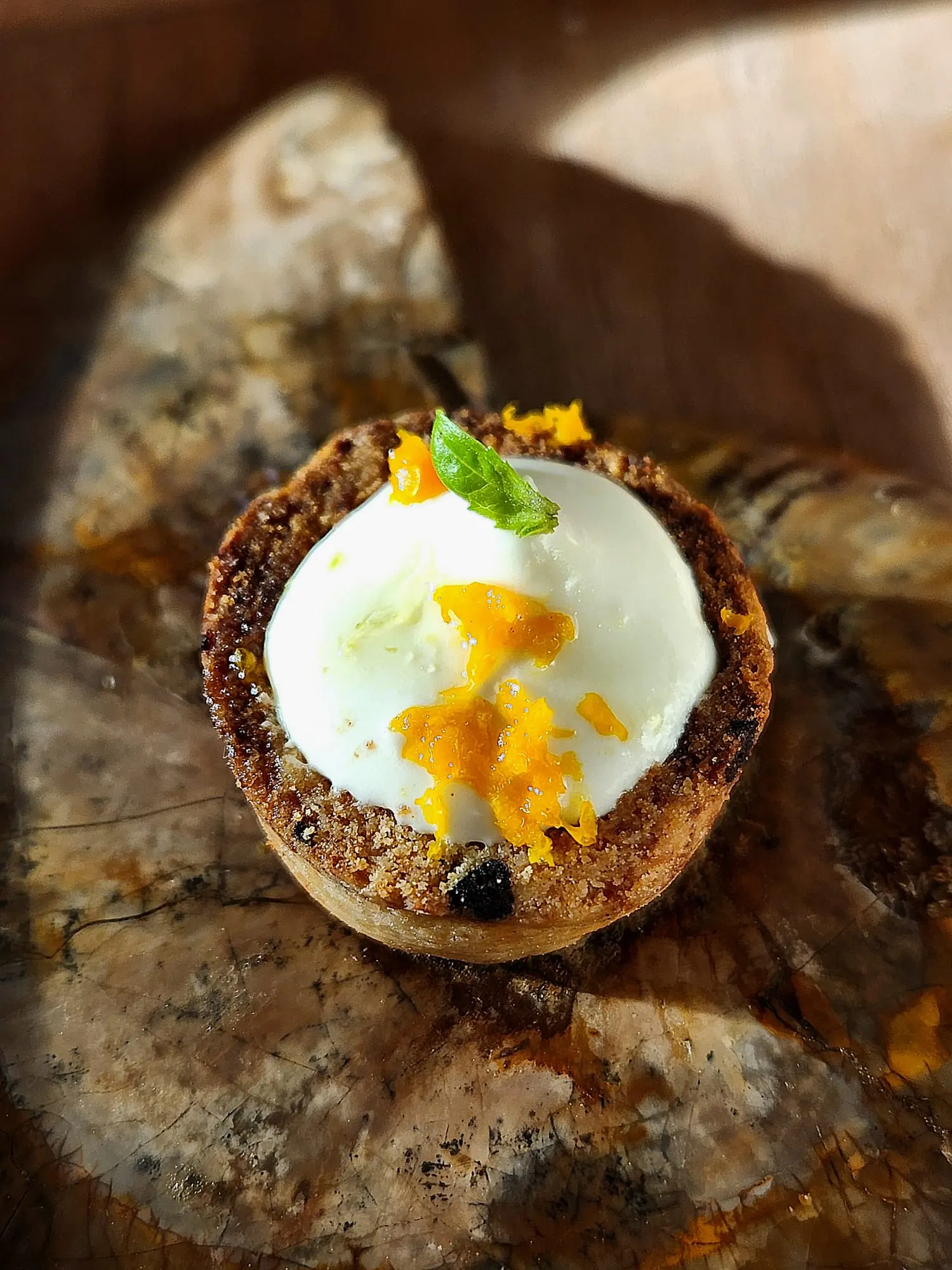 Un dessert dressé par Marie : une boule de crème blanche, du gel orange et un croustillant, sur une planche sombre